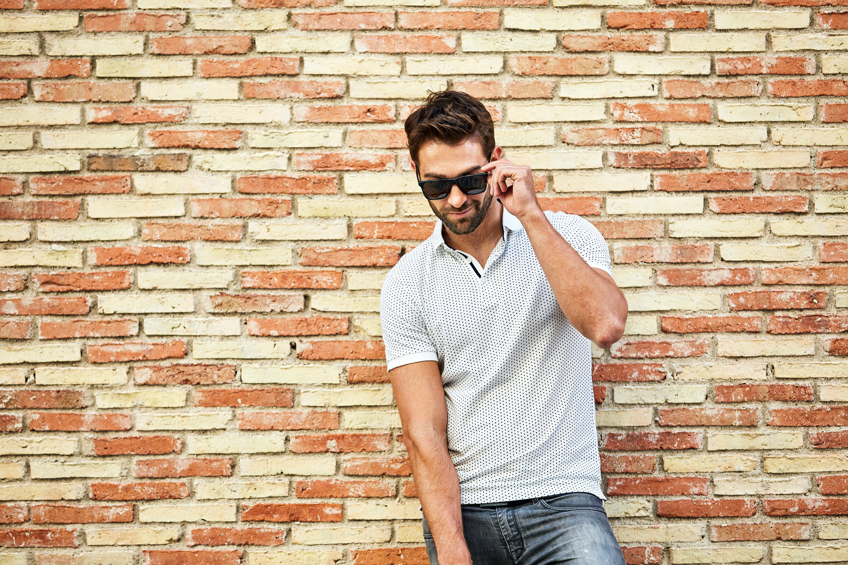 Buy stock photo Shot of a man talking on his cellphone while leaning against a brick wall