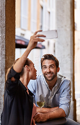 Buy stock photo Shot of a happy couple taking a selfie while sitting outside at a restaurant