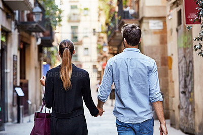 Buy stock photo Shot of an affectionate young couple walking hand in hand together in the city
