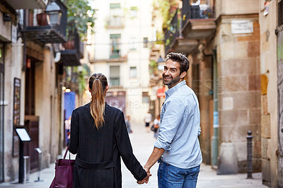 Buy stock photo Shot of an affectionate young couple walking hand in hand together in the city