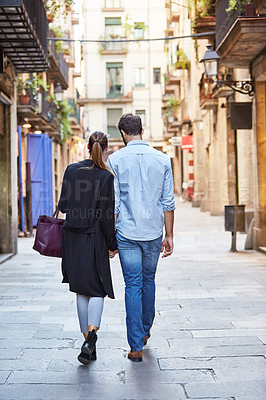 Buy stock photo Shot of an affectionate young couple walking hand in hand together in the city