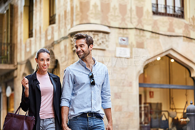 Buy stock photo Shot of an affectionate young couple walking hand in hand together in the city