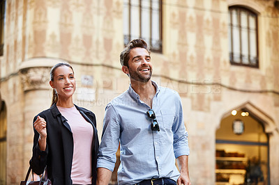 Buy stock photo Shot of an affectionate young couple walking hand in hand together in the city