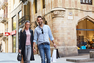 Buy stock photo Shot of an affectionate young couple walking hand in hand together in the city
