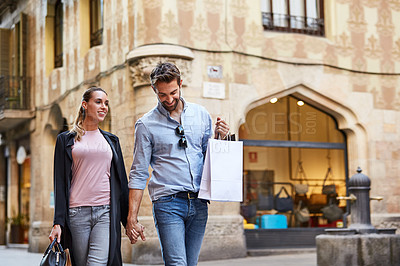 Buy stock photo Shot of an affectionate young couple walking hand in hand together in the city