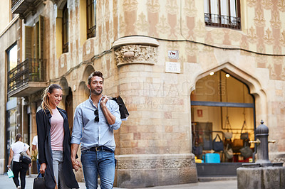 Buy stock photo Shot of an affectionate young couple walking hand in hand together in the city