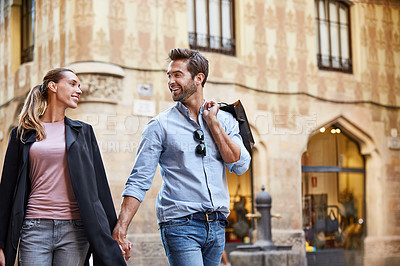Buy stock photo Shot of an affectionate young couple walking hand in hand together in the city