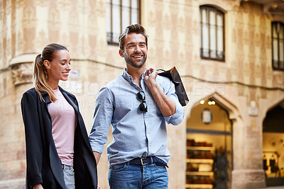 Buy stock photo Shot of an affectionate young couple walking hand in hand together in the city