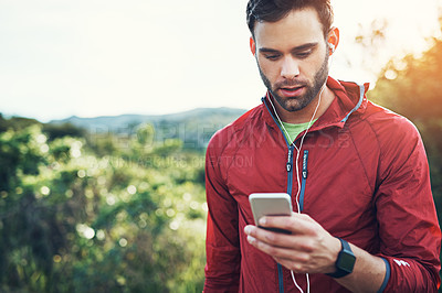 Buy stock photo Cropped shot of a handsome young male athlete checking his cellphone while out for a morning run