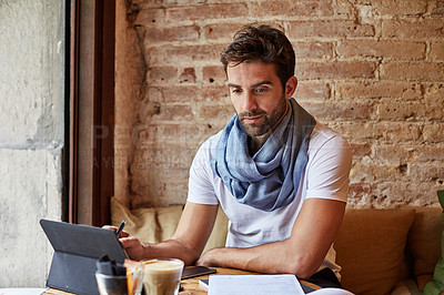 Buy stock photo Shot of a handsome young man using his digital tablet while sitting in a cafe