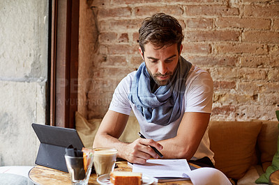 Buy stock photo Shot of a handsome young man using his digital tablet while sitting in a cafe