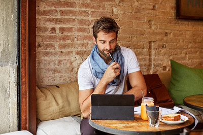 Buy stock photo Shot of a handsome young man using his digital tablet while sitting in a cafe