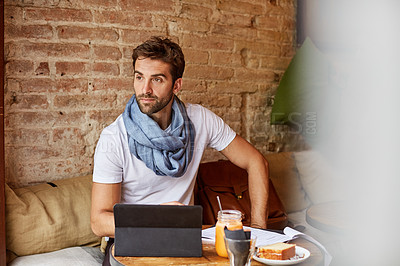 Buy stock photo Shot of a handsome young man using his digital tablet while sitting in a cafe