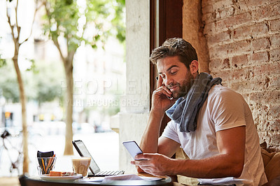 Buy stock photo Shot of a handsome young man using his cellphone while sitting in a cafe