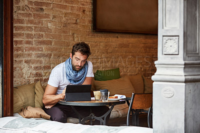 Buy stock photo Shot of a handsome young man using his digital tablet while sitting in a cafe