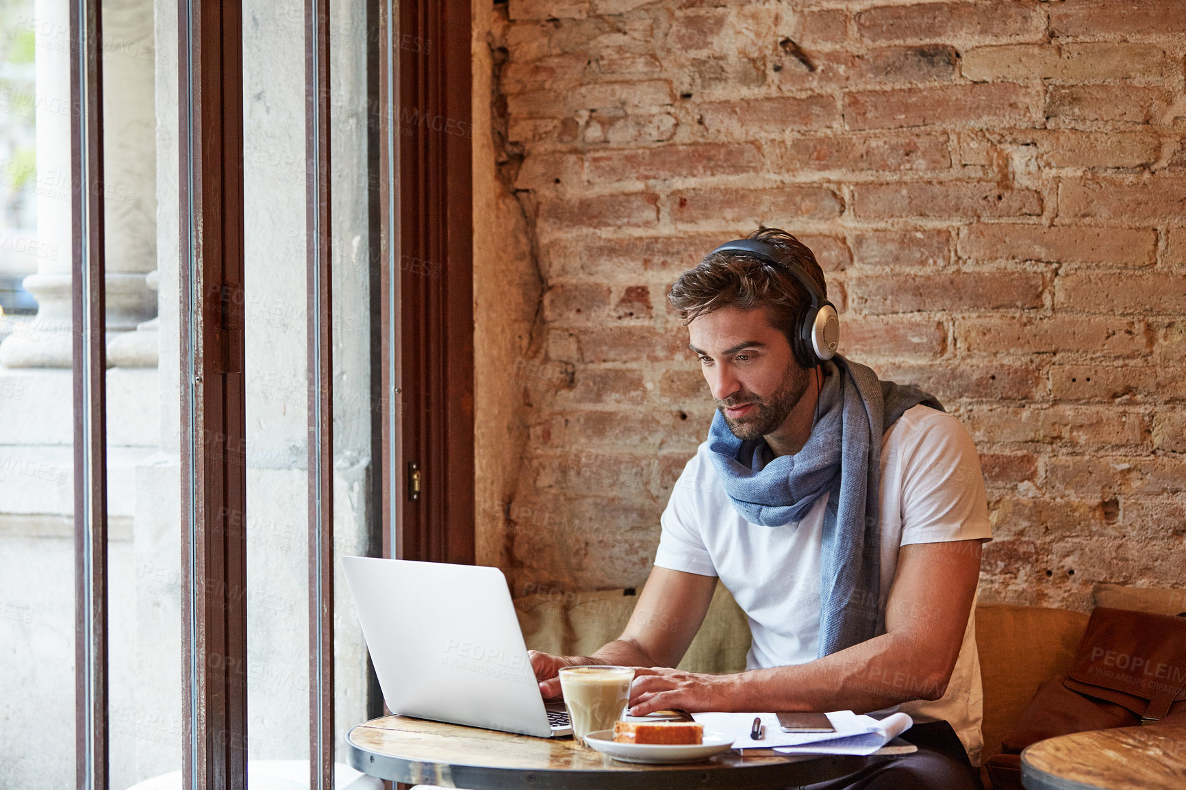 Buy stock photo Remote work, headphones and man with laptop in coffee shop, online or editing video on social media. Content creation, freelancer and person with technology, creative and streaming music in cafe