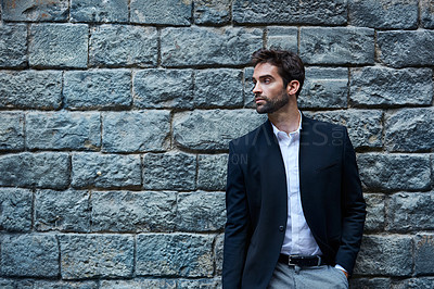 Buy stock photo Cropped shot of a handsome young businessman standing against a brick wall in an urban alleyway