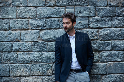 Buy stock photo Cropped shot of a handsome young businessman standing against a brick wall in an urban alleyway