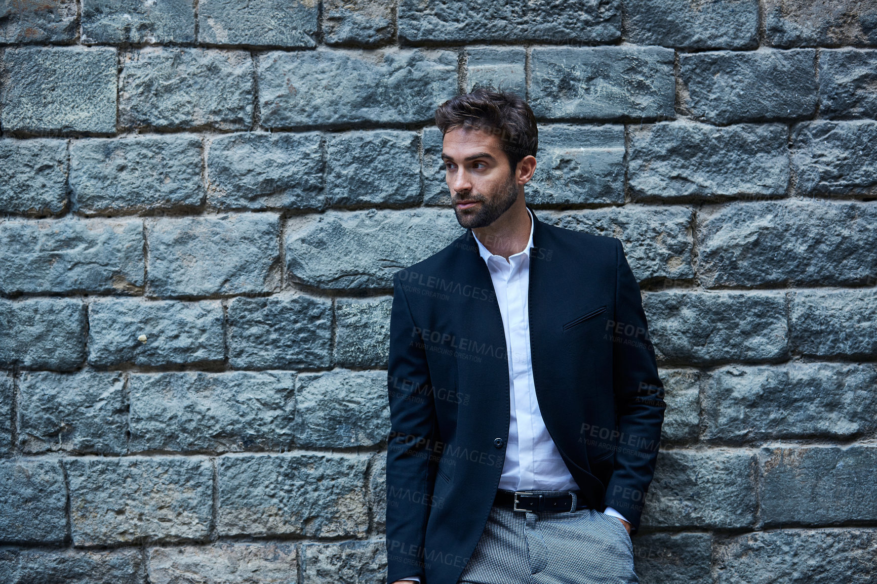 Buy stock photo Cropped shot of a handsome young businessman standing against a brick wall in an urban alleyway
