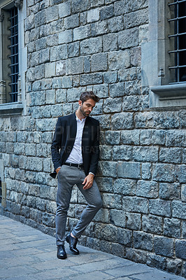 Buy stock photo Full length shot of a handsome young businessman standing against a brick wall in an urban alleyway