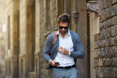 Buy stock photo Cropped shot of a handsome young businessman sending a text while walking through an urban alleyway