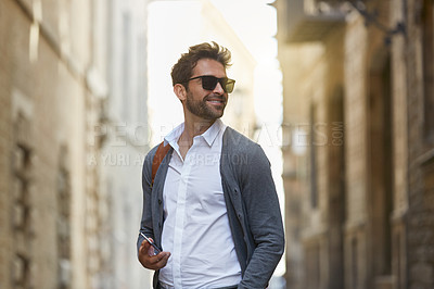 Buy stock photo Cropped shot of a handsome young businessman sending a text while walking through an urban alleyway