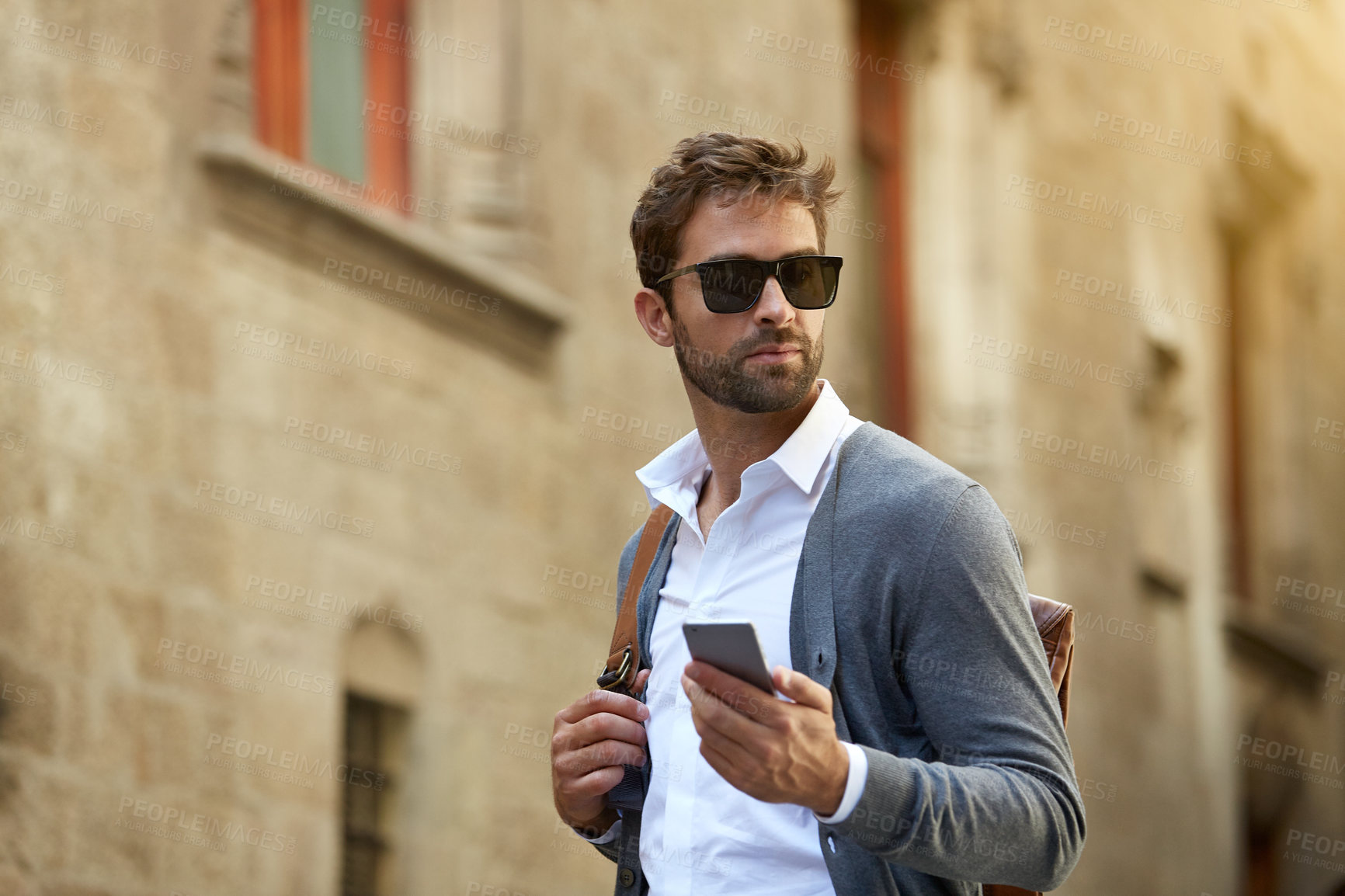 Buy stock photo Cropped shot of a handsome young businessman checking his messages while walking through an urban alleyway