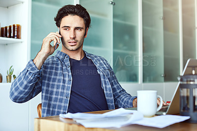 Buy stock photo Shot of a focused young man talking on his phone while working inside at home