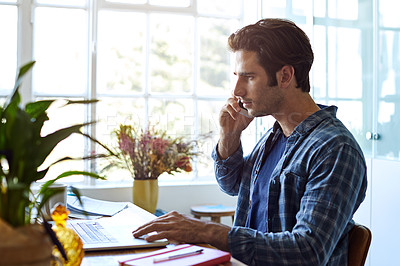 Buy stock photo Shot of a focused young man talking on his phone while working inside at home