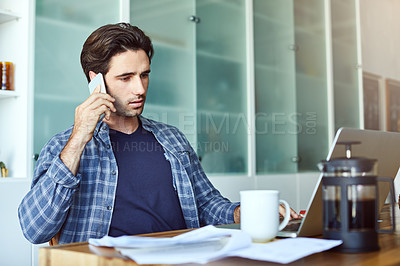 Buy stock photo Shot of a focused young man talking on his phone while working inside at home