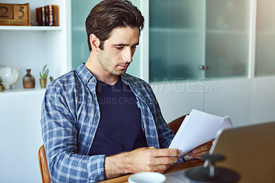 Buy stock photo Shot of a focused young man doing paperwork at home while drinking coffee