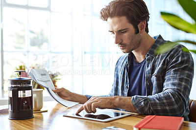 Buy stock photo Shot of a focused young man working on his digital tablet while being seated next to a table at home