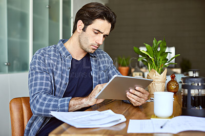 Buy stock photo Cropped shot of a handsome young man using a tablet while working from home