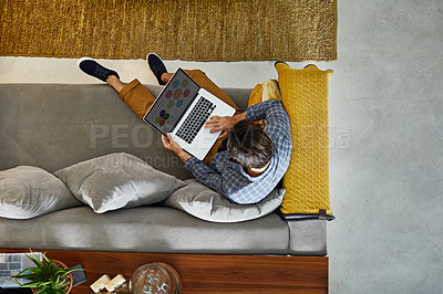 Buy stock photo High angle shot of a focused young unrecognizable man working on a laptop while relaxing on a couch at home