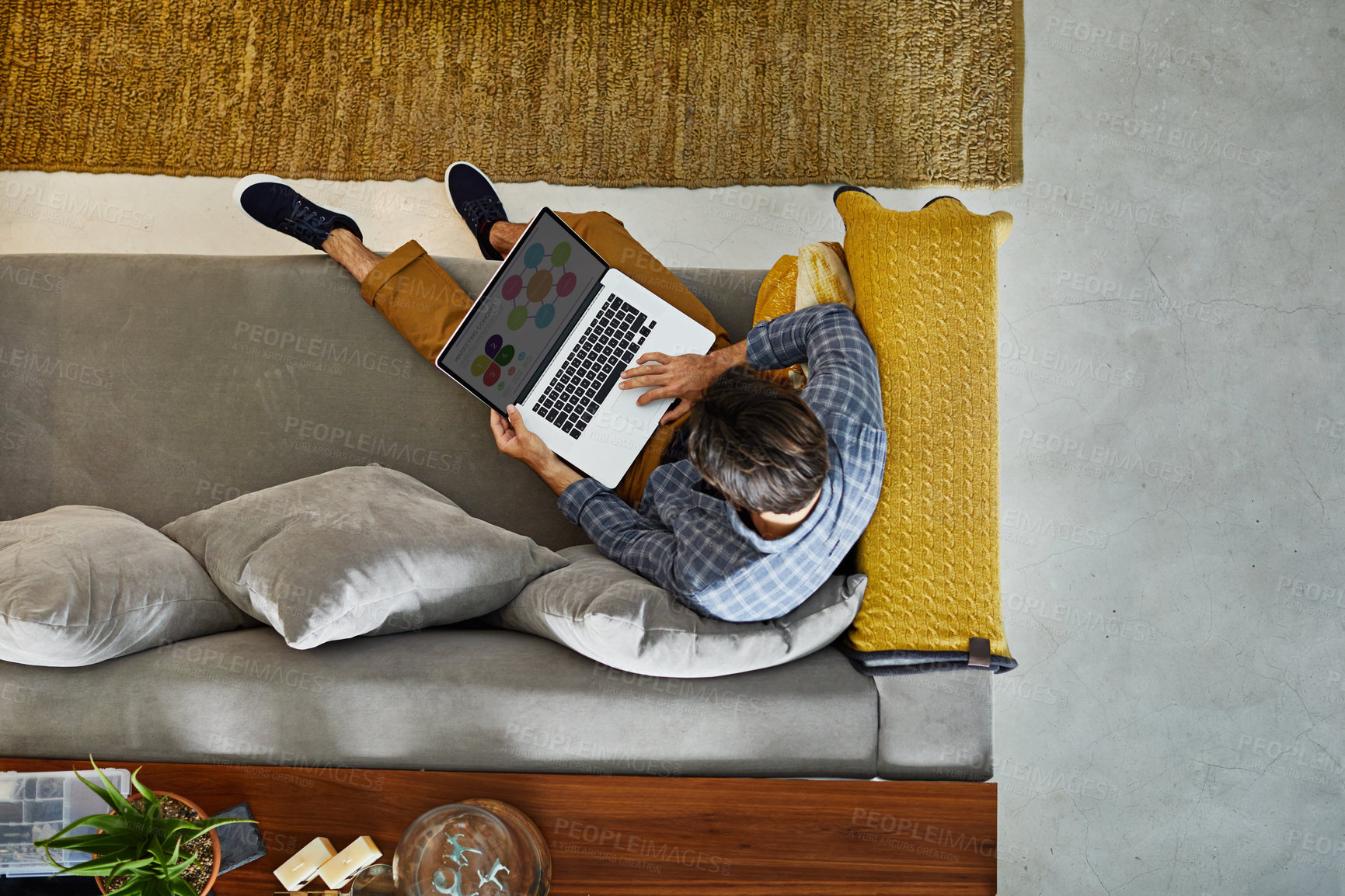 Buy stock photo High angle shot of a focused young unrecognizable man working on a laptop while relaxing on a couch at home
