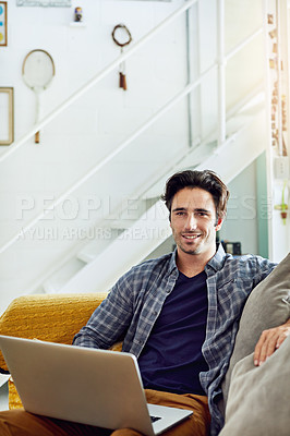 Buy stock photo Portrait of a cheerful young man working on a laptop while being seated on a couch at home