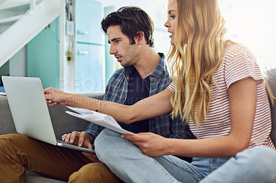 Buy stock photo Shot of a focused young couple working together on a laptop while being seated on a couch at home
