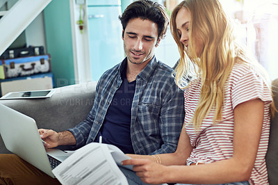 Buy stock photo Shot of a focused young couple working together on a laptop while being seated on a couch at home