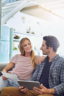 Buy stock photo Shot of a cheerful young couple working together on a digital tablet while being seated on a couch at home