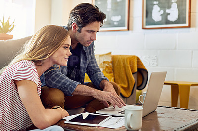 Buy stock photo Shot of a focused young couple working together on a laptop while being seated on a couch at home