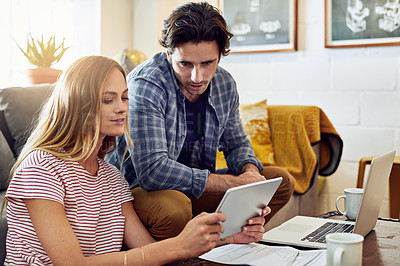 Buy stock photo Shot of a focused young couple working together on a digital tablet while being seated on a couch at home