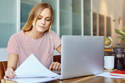 Buy stock photo Shot of a focused young woman working on a laptop while doing paperwork inside at home