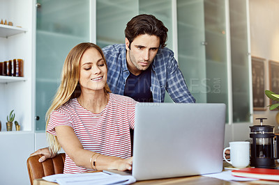 Buy stock photo Shot of a focused young couple working together on a laptop while being seated next to table at home