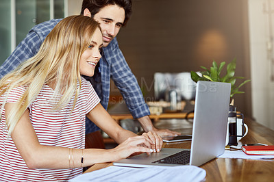 Buy stock photo Shot of a cheerful young couple working together on a laptop while being seated next to table at home