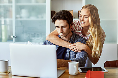 Buy stock photo Shot of a focused young couple working together on a laptop while being seated next to table at home