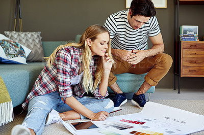 Buy stock photo Shot of a focused young couple drawing plans and choosing colors for the renovation of their house while being seated on the floor