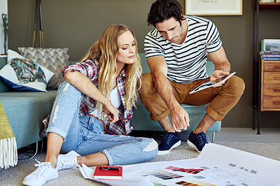 Buy stock photo Shot of a focused young couple drawing plans and choosing colors for the renovation of their house while being seated on the floor