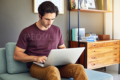 Buy stock photo Shot of a handsome young man using his laptop on the sofa at home