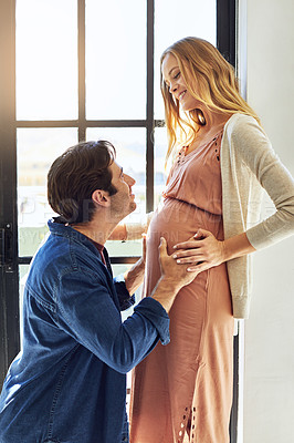 Buy stock photo Shot of a young man feeling his pregnant wife's tummy at home