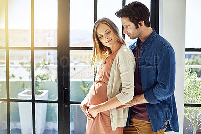 Buy stock photo Shot of a young man embracing his pregnant wife at home